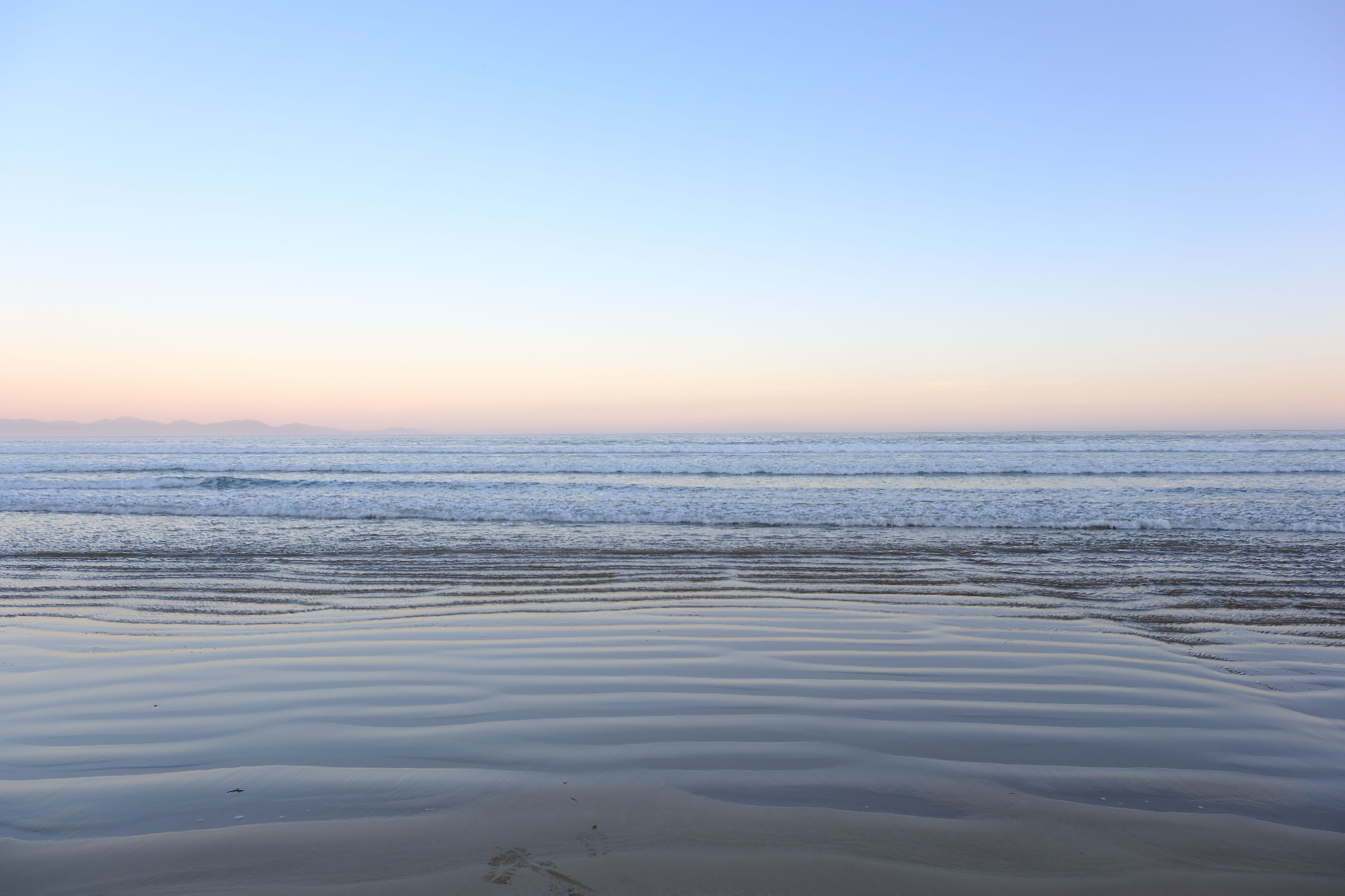 Calm beach at sunrise with gentle waves and soft pastel sky