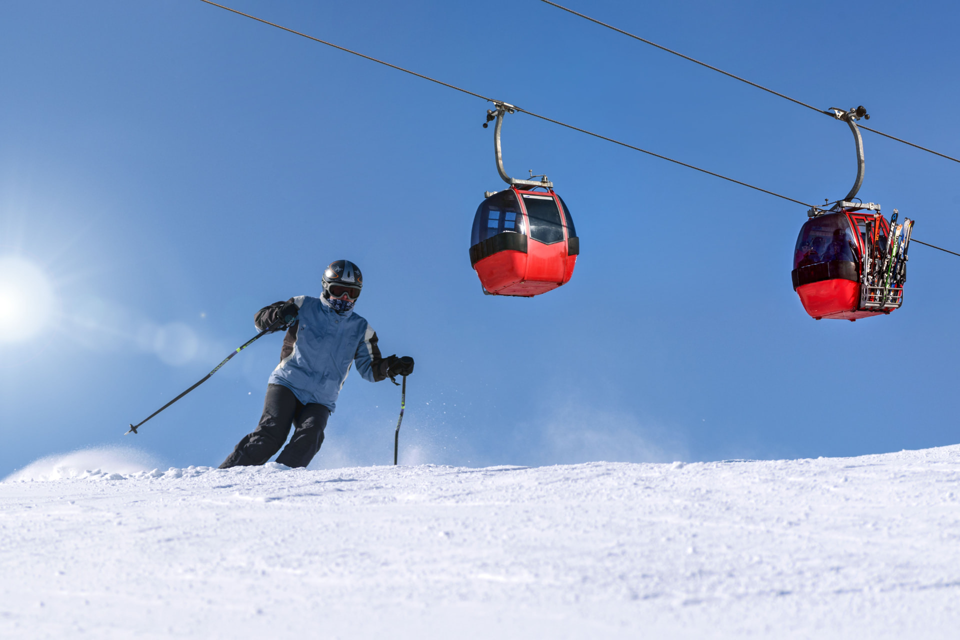 A skier on a snowy slope beneath red gondola lifts